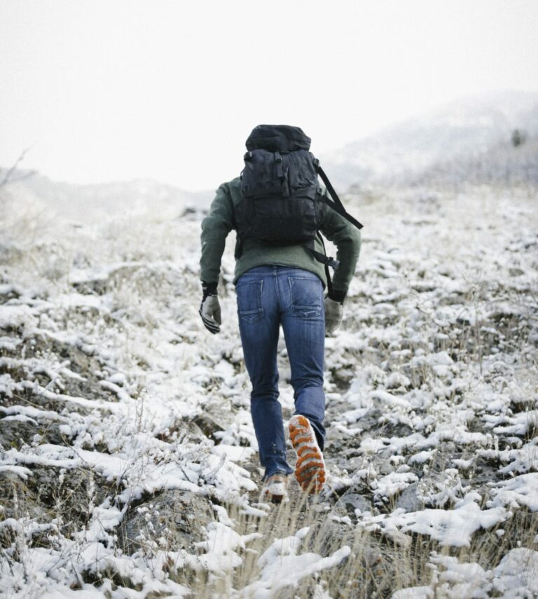 Man hiking up a steep mountain covered in snow while carrying a backpack