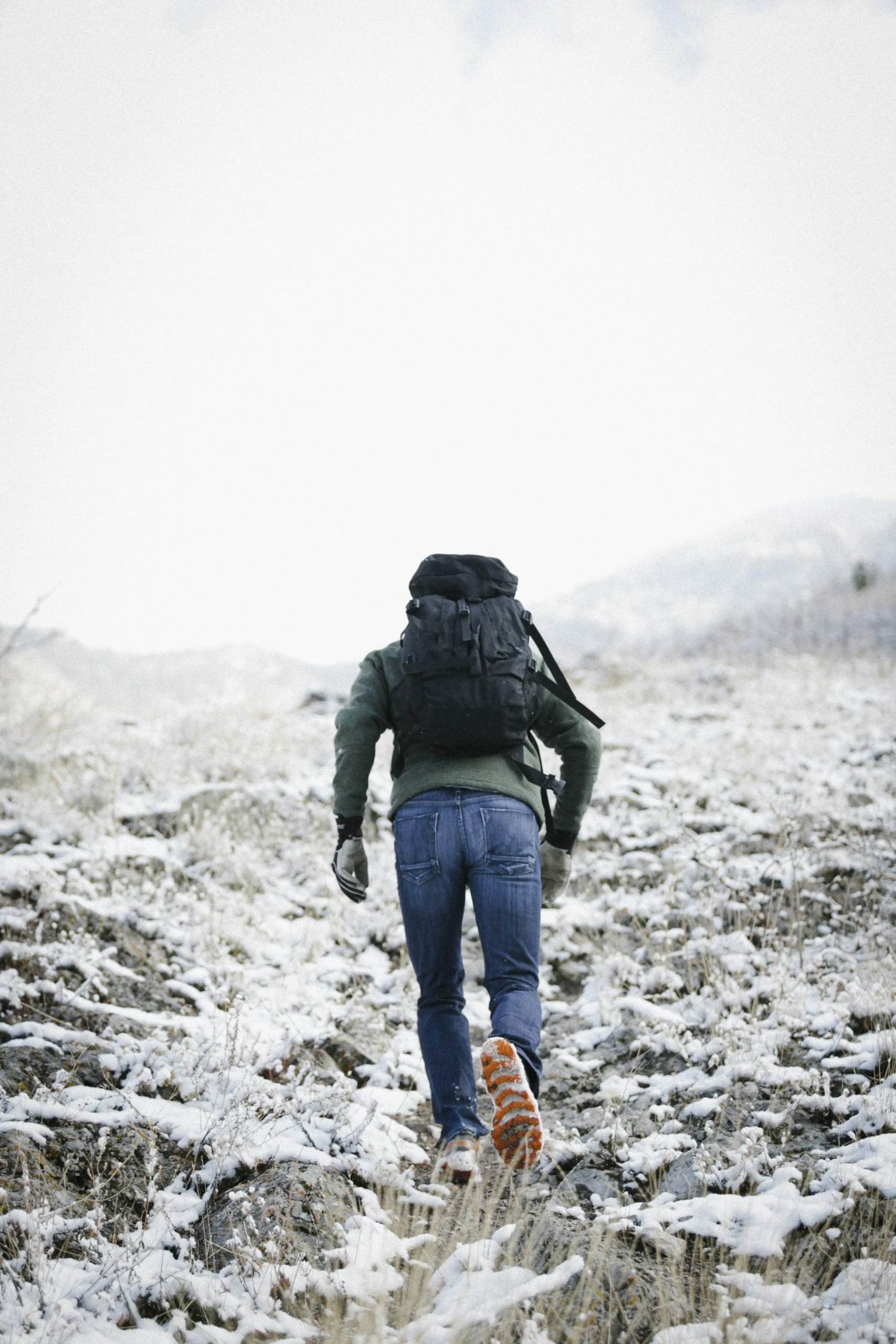 Man hiking up a steep mountain covered in snow while carrying a backpack