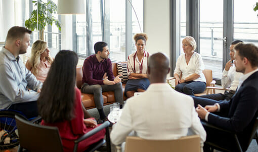 A group of diverse people sitting in chairs in a circle, having conversation.